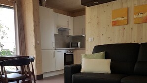 Un espace de vie compact comprenant un canapé noir, une table basse en bois, une table à manger avec des chaises et une kitchenette équipée d’un four à micro-ondes et d’un four traditionnel.