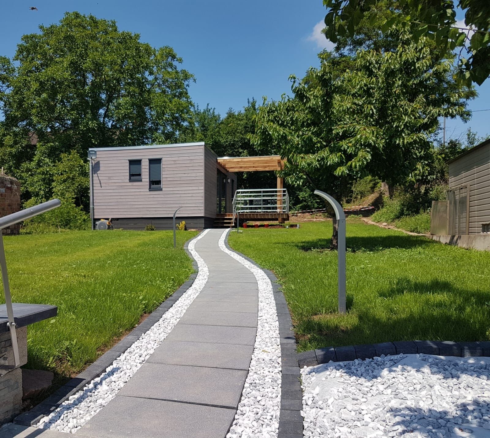 A pathway leading to a modern building with a covered outdoor area and a small structure.