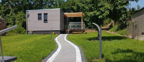 A pathway leading to a modern building with a covered outdoor area and a small structure.
