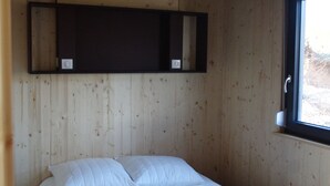 Un lit simple avec une couette blanche matelassée et une serviette pliée posée dessus. Il y a une étagère en bois au-dessus du lit.