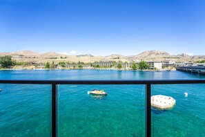 A clear view of a lake with a boat in the foreground, surrounded by buildings and hills in the background. - Grandview 720 Waterfront King with River View (Chelan)
