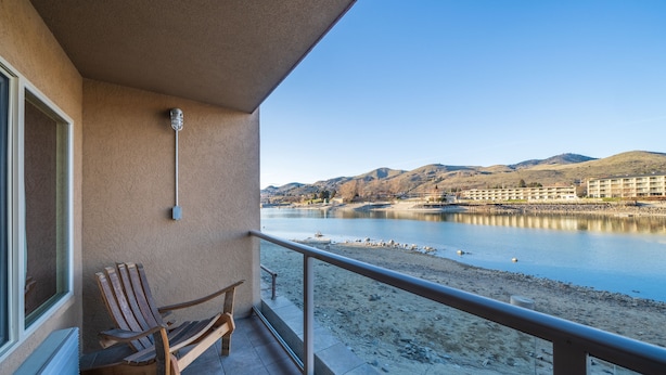 A balcony with a wooden chair, a view of a lake, and a distant building. - Grandview 710 Waterfront King with River View (Chelan)