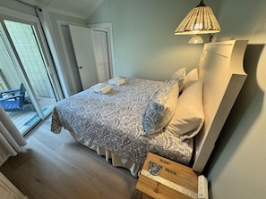 Un dormitorio con cama, mesita de noche, lámpara y vistas al exterior.