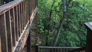 A wooden staircase leading down to a forested area with a wooden railing and a metal bell.
