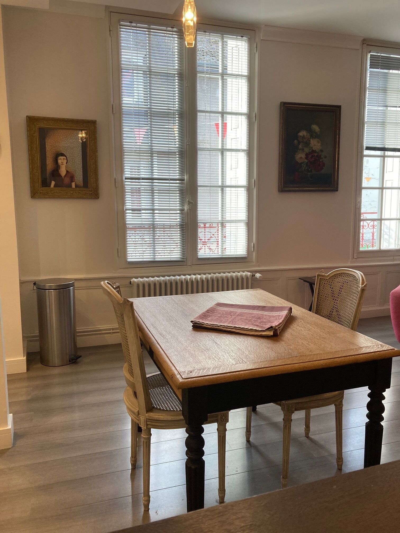 Uma sala de jantar com mesa e cadeiras de madeira, um radiador e duas janelas com persianas.
