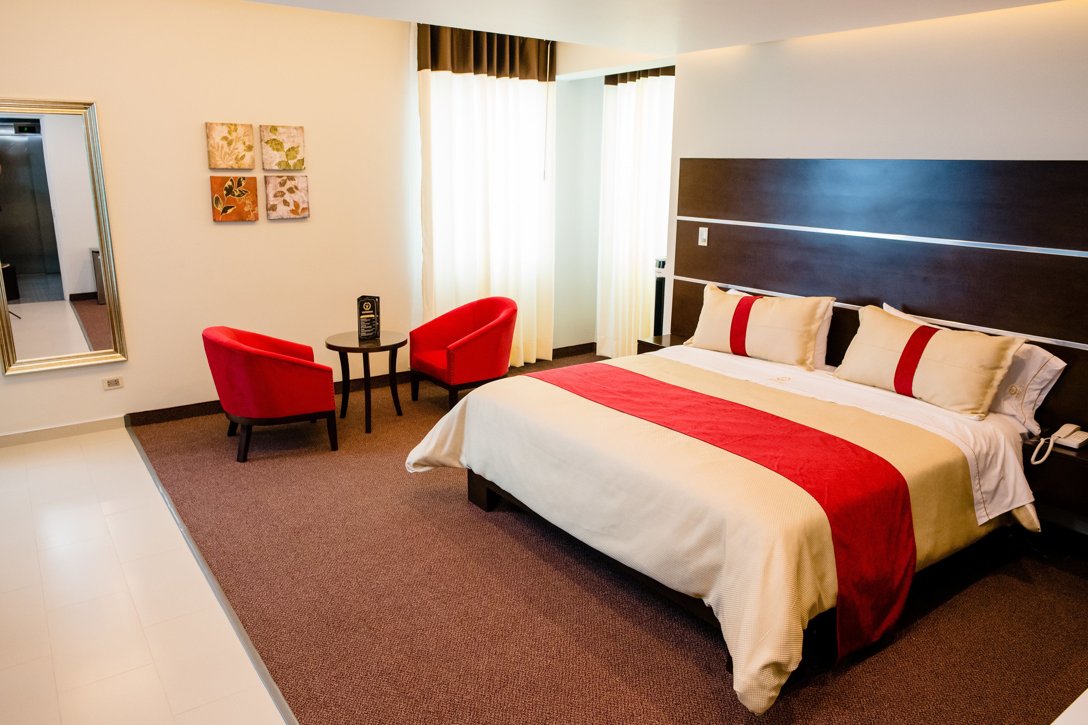 Habitació d'hotel amb un llit gran, un butaca vermella, una taula petita i un mirall.