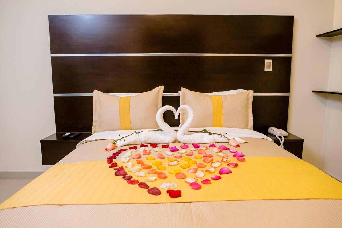 A hotel room with a bed, a headboard, a bedside table, and a phone.