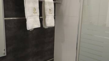 Un baño con inodoro, toallero y dos toallas, además de una cabina de ducha con mampara de vidrio.