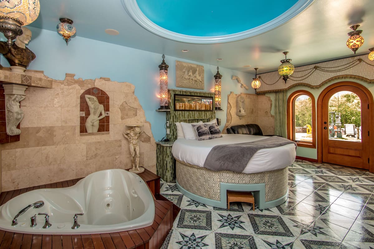 A luxurious bedroom with a large bathtub, a bed with patterned bedding, and decorative wall art.