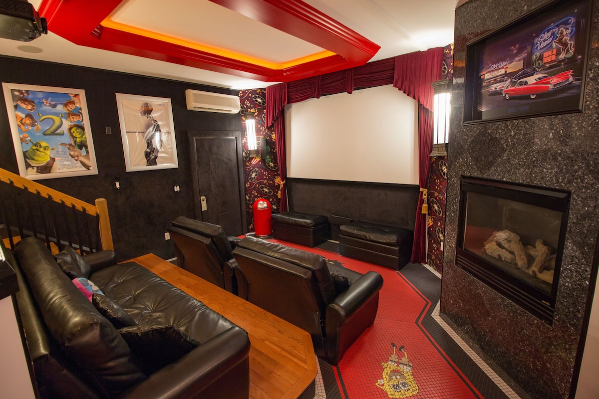 A theater room with a red carpet, black leather seating, a wooden table, and a fireplace.