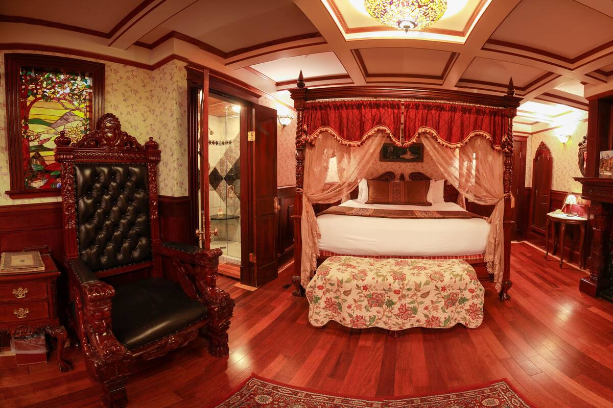 A traditional bedroom with a four-poster bed, a canopy, a fireplace, and ornate furniture.