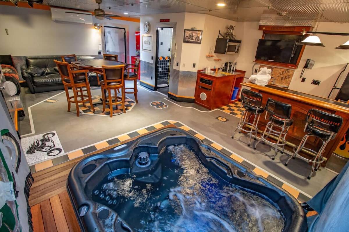 A room with a hot tub, a dining area with chairs, a bar with stools, and a sofa.