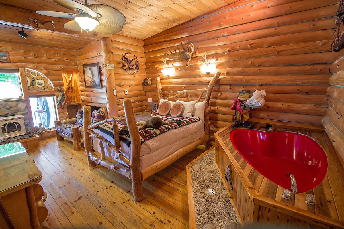 A cozy log cabin interior with a bed, a red sink, and a fireplace.