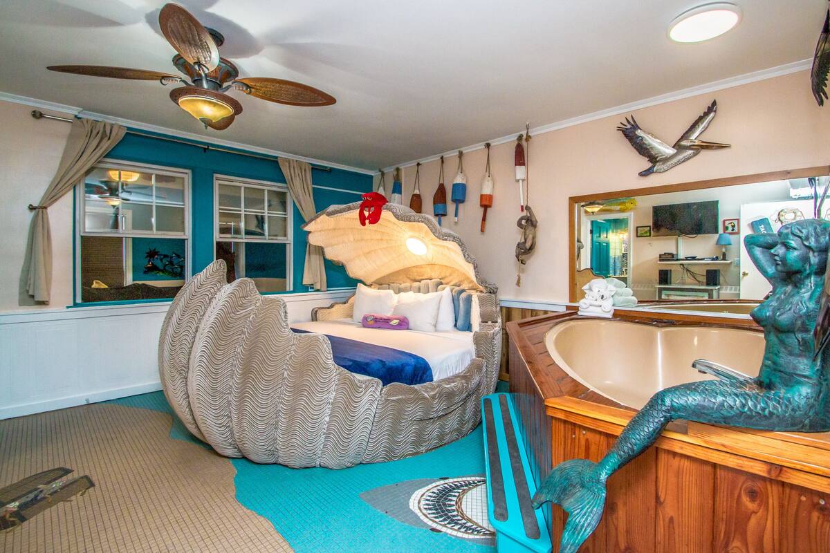 A bedroom with a bed in a boat-shaped pod, a wooden bathtub, and a ceiling fan.