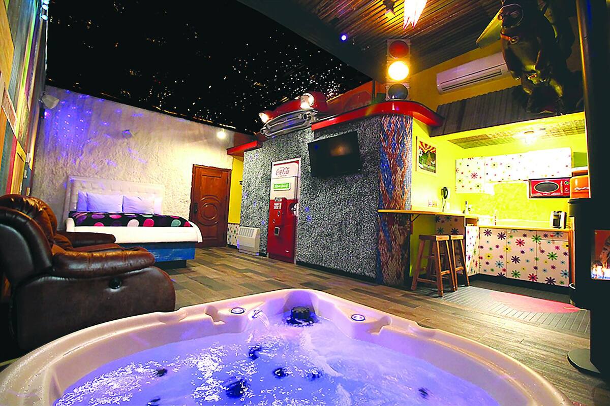 A room with a hot tub, a bed, a sofa, a small kitchen area, and a wall with a Coca-Cola sign.