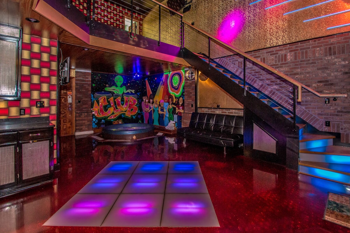 A modern interior with a dance floor, a staircase, and a graffiti wall.