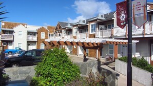 A residential area with a row of townhouses, a covered patio, and a flagpole with banners. - Luxury Condo at the Arch in the heart of Historic Nye Beach (Newport)