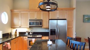 A kitchen with wooden cabinets, a stainless steel refrigerator, a microwave, a stove, and a black granite countertop. - Luxury Condo at the Arch in the heart of Historic Nye Beach (Newport)