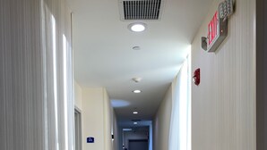 A long, narrow hotel corridor with a sign indicating room number 615, a fire alarm, and a ceiling vent.