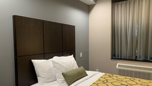 A hotel room with a large bed, a headboard, a window with curtains, and a radiator.
