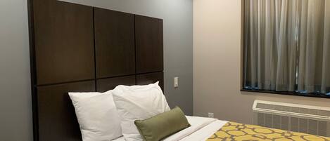 Ein Hotelzimmer mit einem großen Bett, einem Kopfteil, einem Fenster mit Vorhängen und einem Heizkörper.