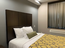 Ein Hotelzimmer mit einem großen Bett, einem Kopfteil, einem Fenster mit Vorhängen und einem Heizkörper.