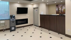 A hotel lobby with a reception desk, a flat-screen TV mounted on the wall, an ATM machine, and a fireplace.