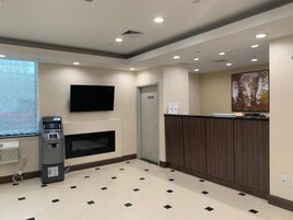 Eine Hotelhalle mit Empfangsschalter, einem an der Wand montierten Flachbildfernseher, einem Geldautomaten und einem Kamin.