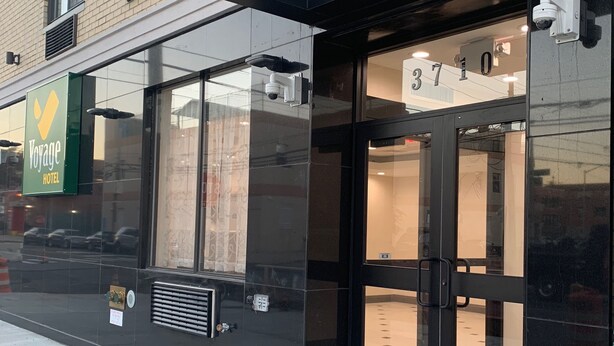 A modern hotel entrance with glass doors, a visible room number, and a security camera.