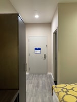 Ein Hotelzimmer mit Schrank, einem Bett mit gemustertem Überwurf, einer Tür mit Brandschutzplan und einer Deckenleuchte.