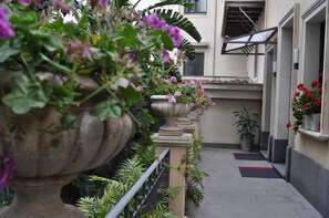 A narrow pathway flanked by large planters with flowers and potted plants, leading to a building entrance. - Ognina Residence (Catania)
