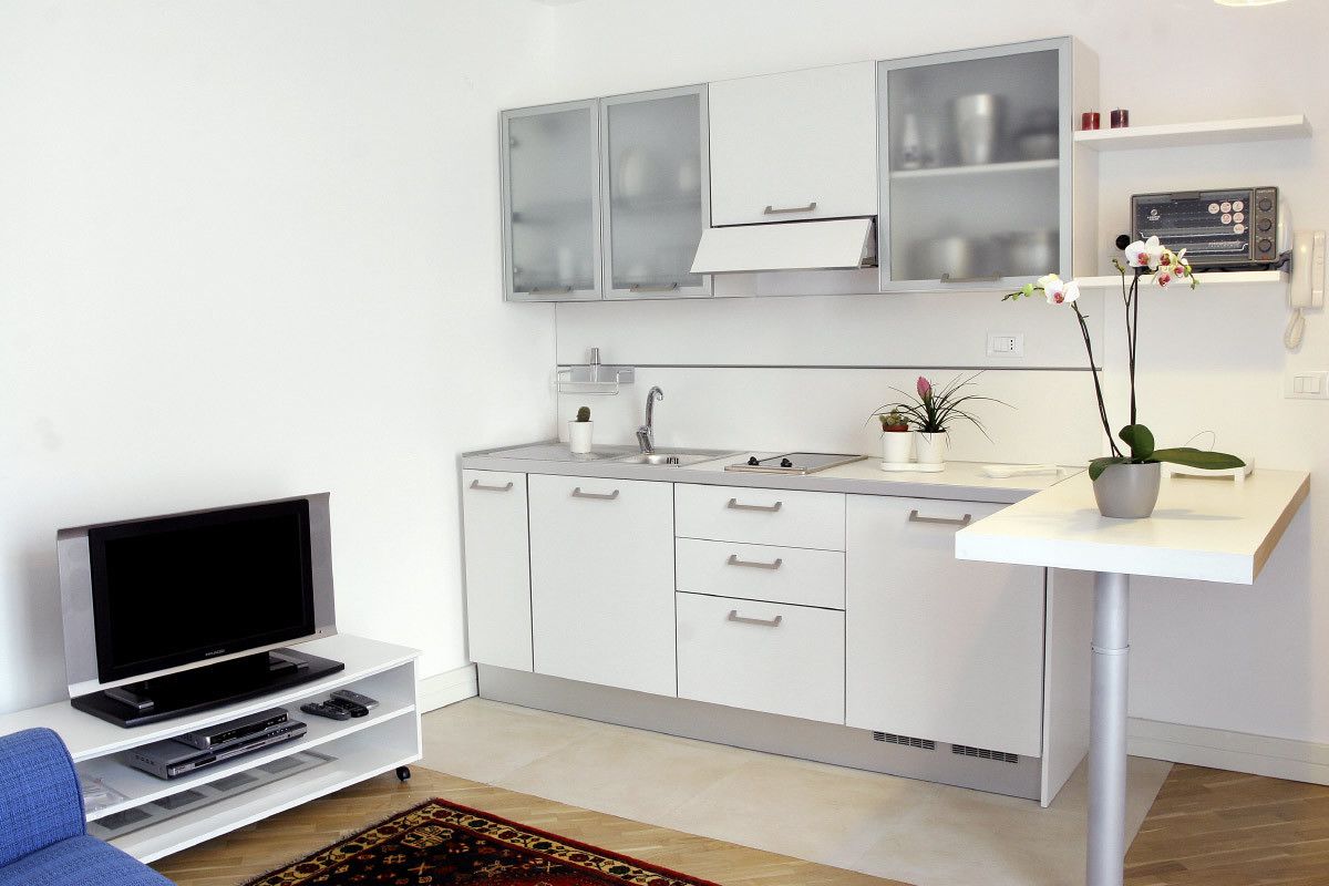 Une cuisine moderne avec des meubles blancs, un four encastré et un petit coin repas comprenant une table et des chaises blanches.