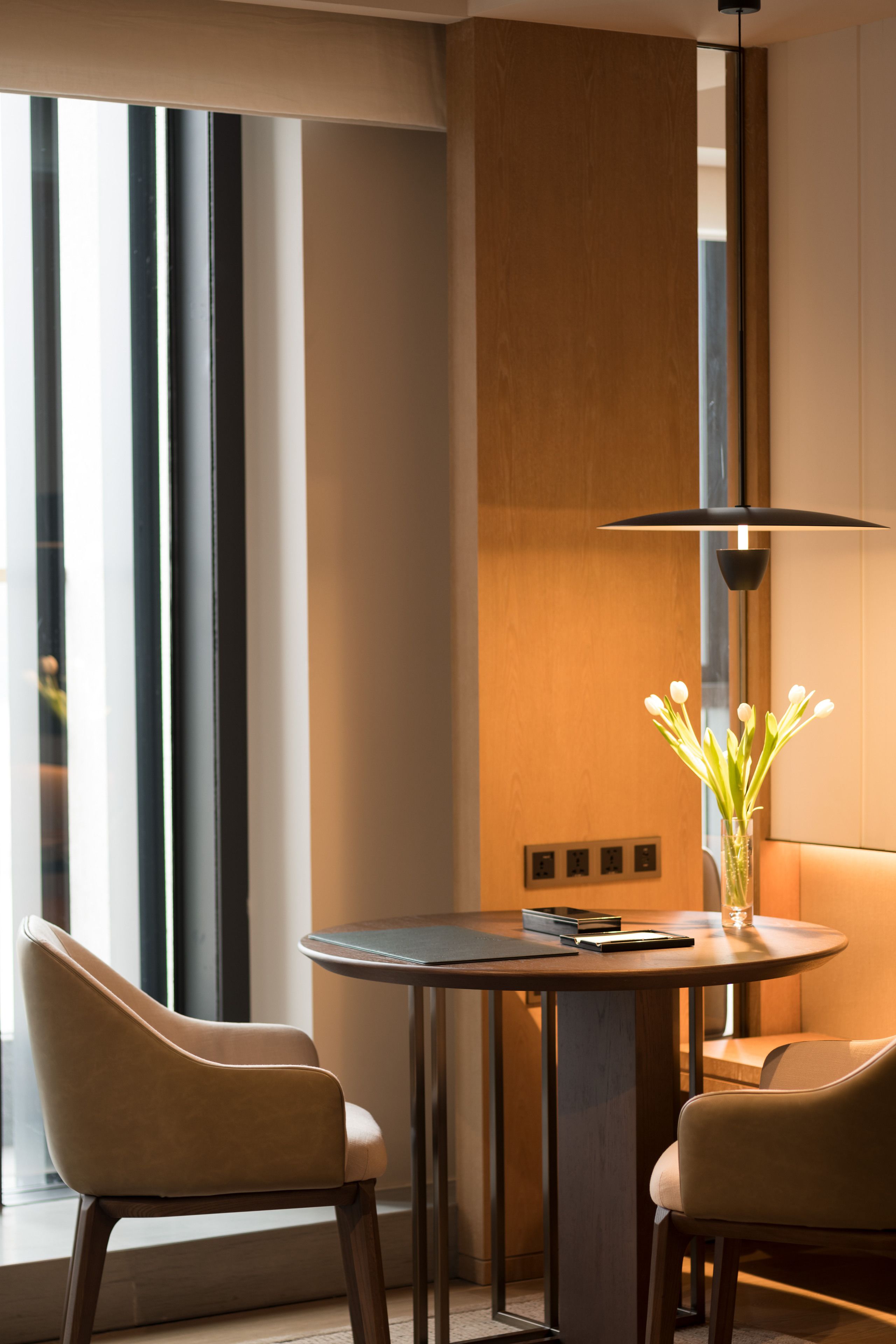 A modern room with a round table, two chairs, a vase with flowers, and a pendant light.
