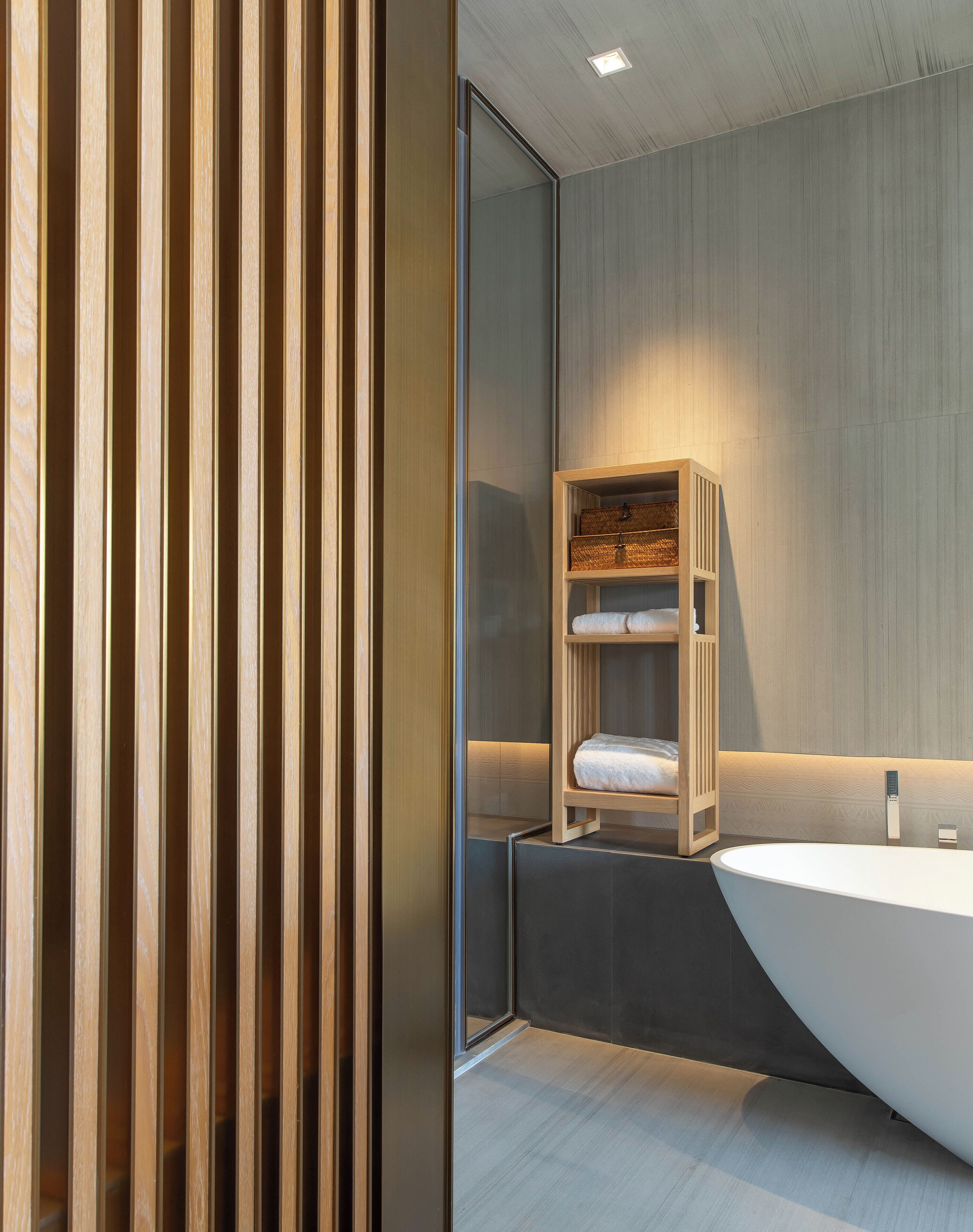 Une salle de bain moderne avec un meuble-lavabo en bois, une grande baignoire et une étagère intégrée où sont rangées les serviettes.