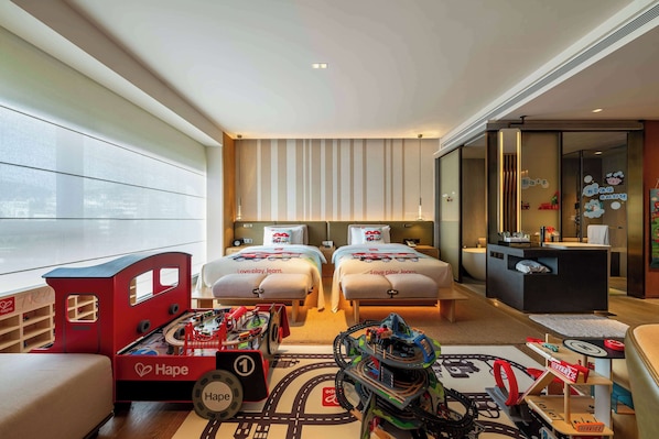 Habitación de hotel con dos camas, un escritorio y una zona de juegos con trenes de juguete.