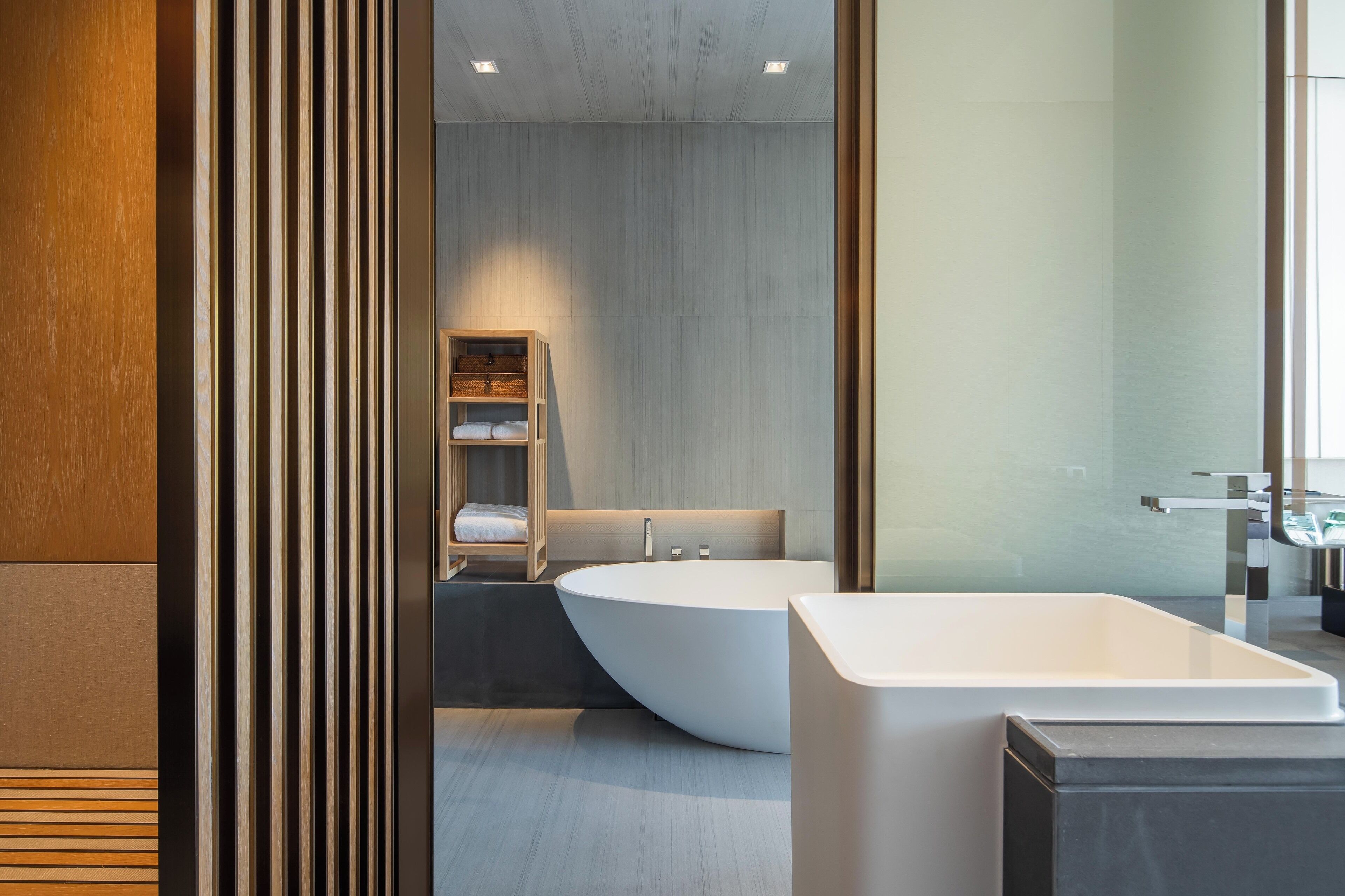 Une salle de bain moderne avec une baignoire sur pieds, un meuble-lavabo en bois et une étagère intégrée où sont rangées les serviettes.