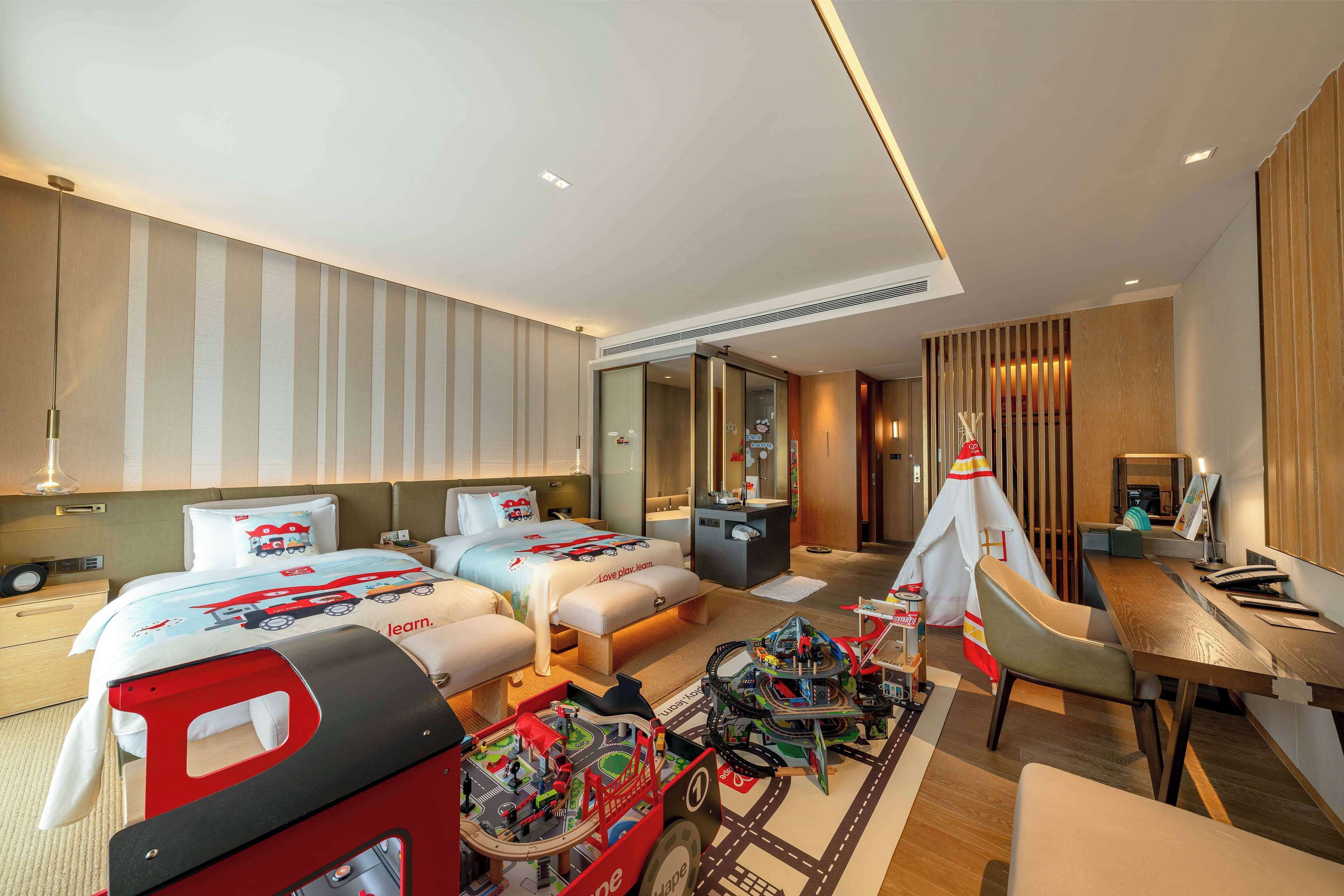 A hotel room with two beds, a desk, a chair, a small table, and a toy train set.