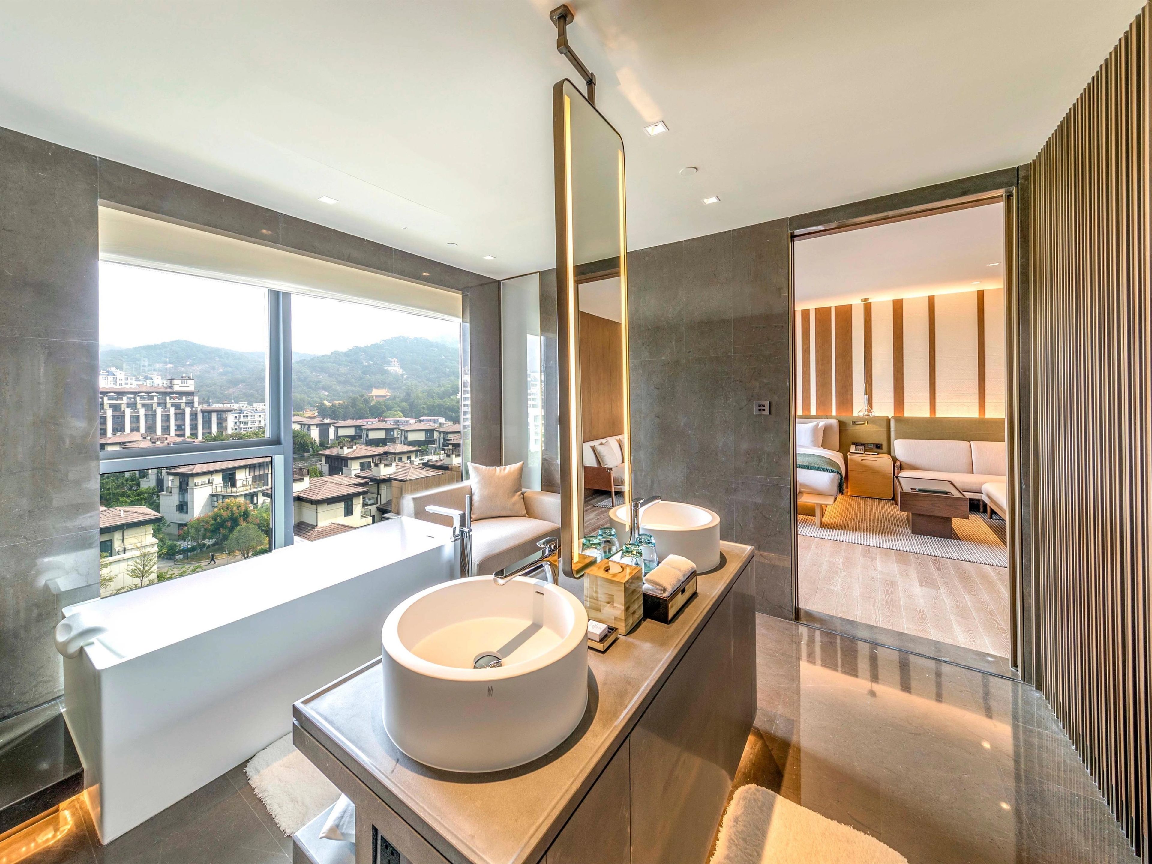 A modern bathroom with a large window, a bathtub, and a vanity with a large sink.