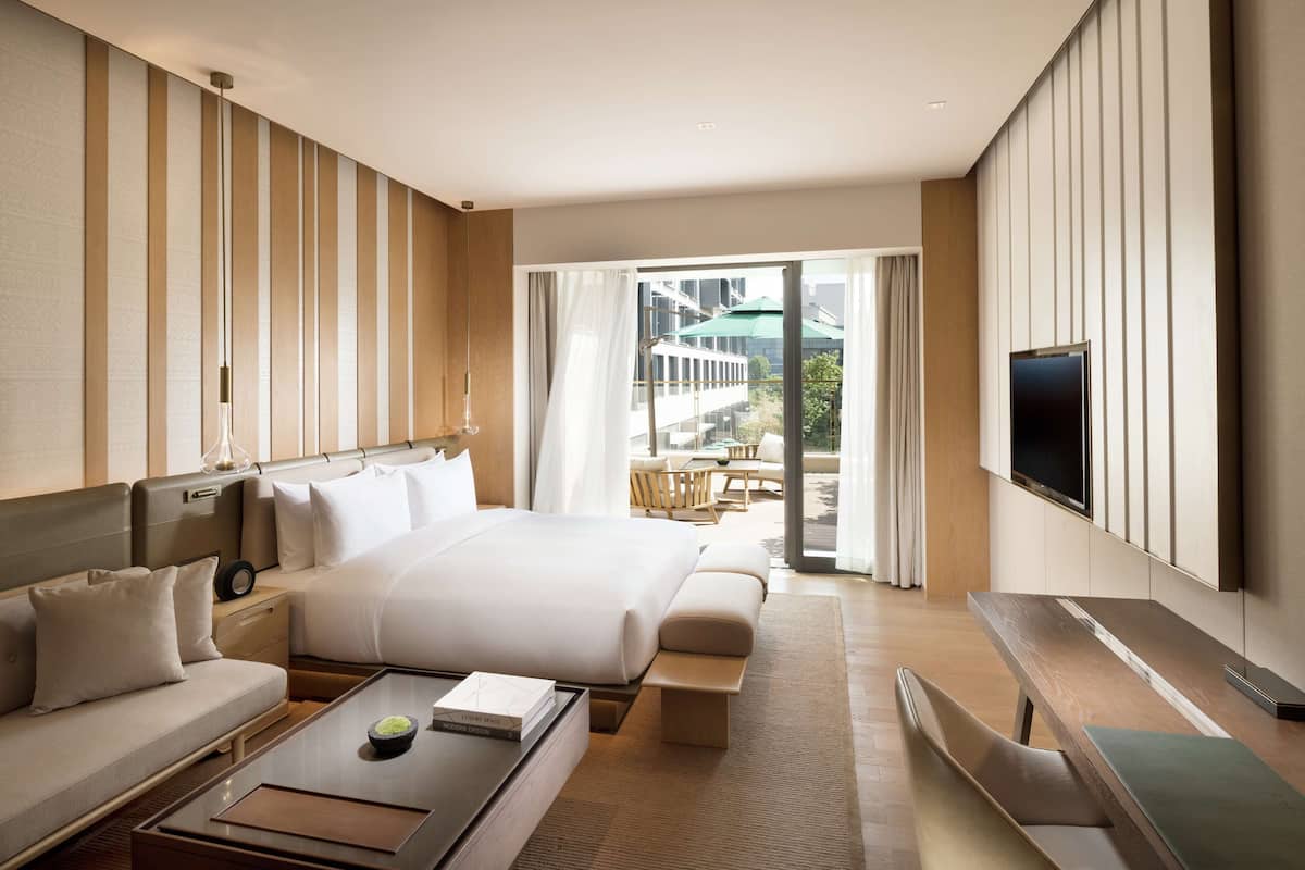 Une chambre d’hôtel moderne dotée d’un grand lit, d’un canapé, d’une table basse, d’une télévision et d’un balcon offrant une vue sur les bâtiments.