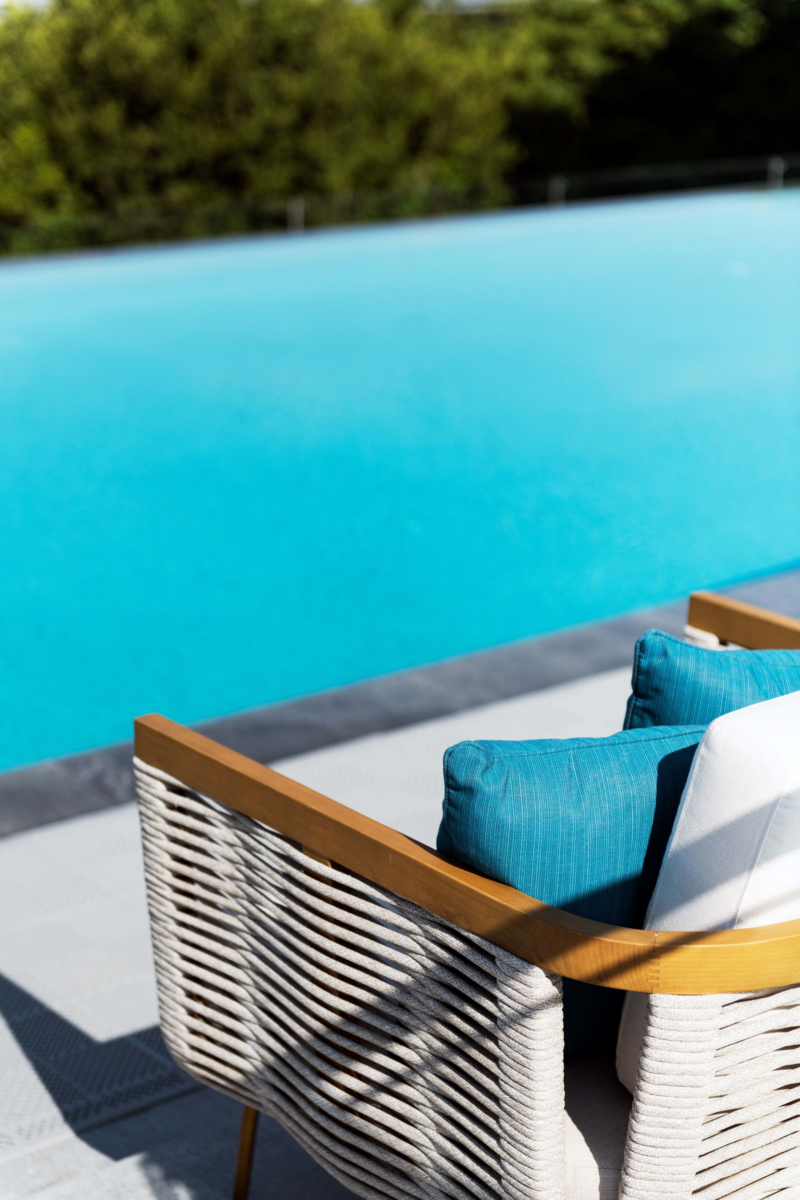 Ein Korbsessel mit Holzgestell und blauen Kissen an einem Pool.