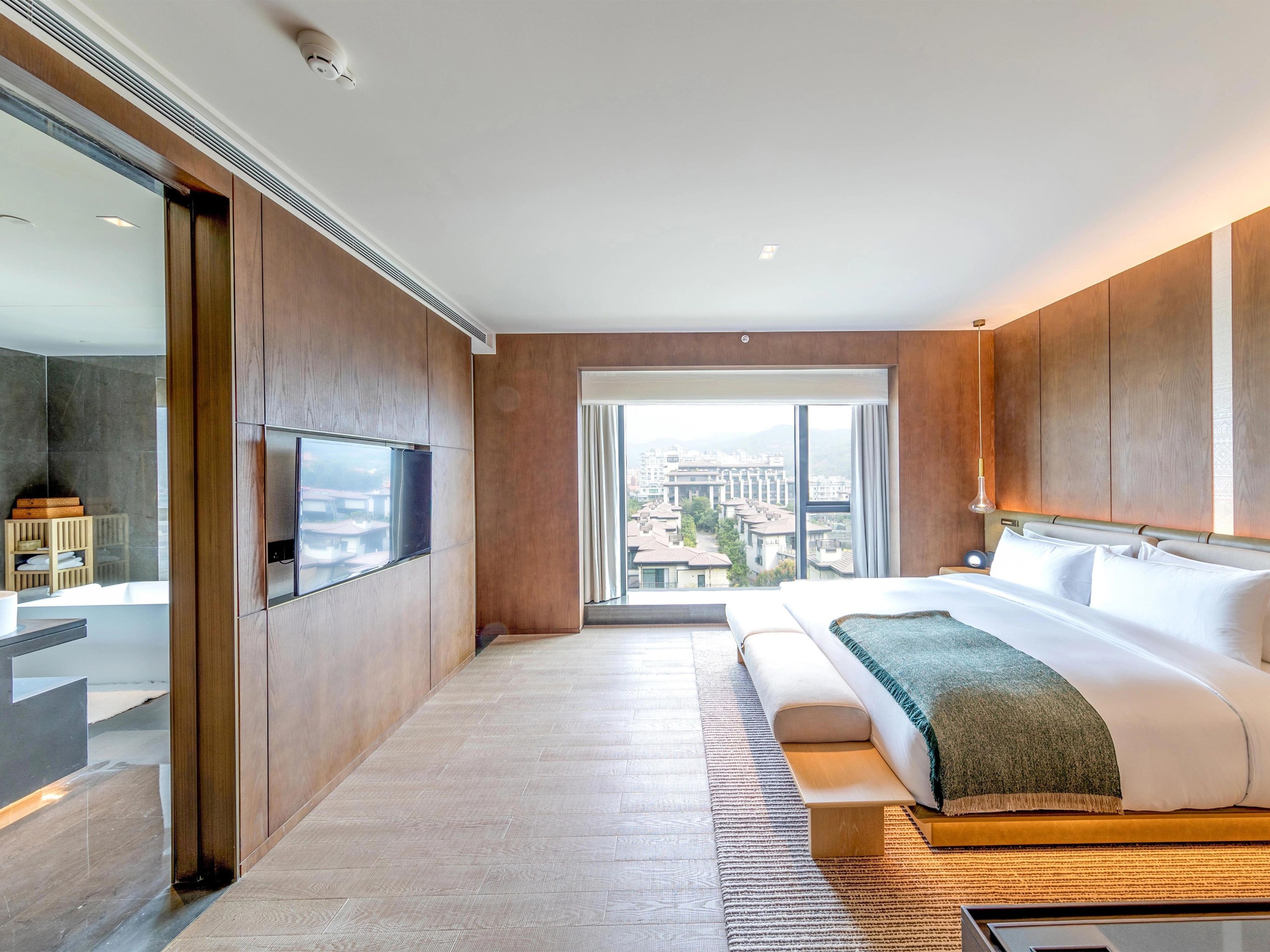 A modern hotel room with a large bed, a TV, and a view of the city.