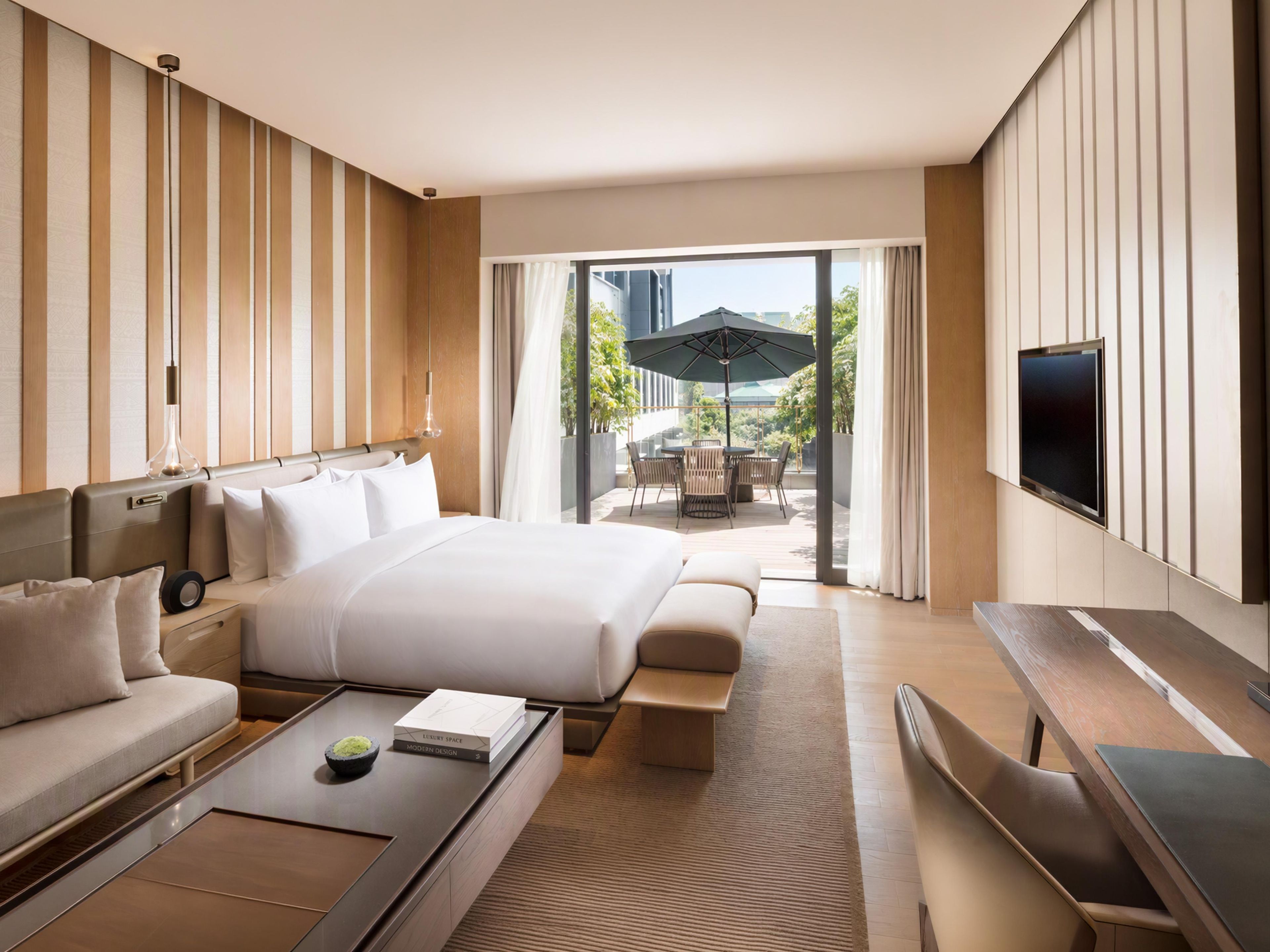 Ein modernes Hotelzimmer mit einem großen Bett, einer Couch, einem Couchtisch, einem Fernseher und einem Balkon mit Gartenmöbeln.