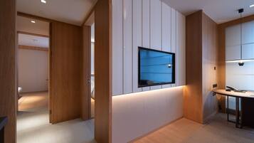 Een moderne hotelkamer met een houten vloer, een bureau met stoel, een flatscreen televisie aan de muur en een groot raam dat voor natuurlijk licht zorgt.