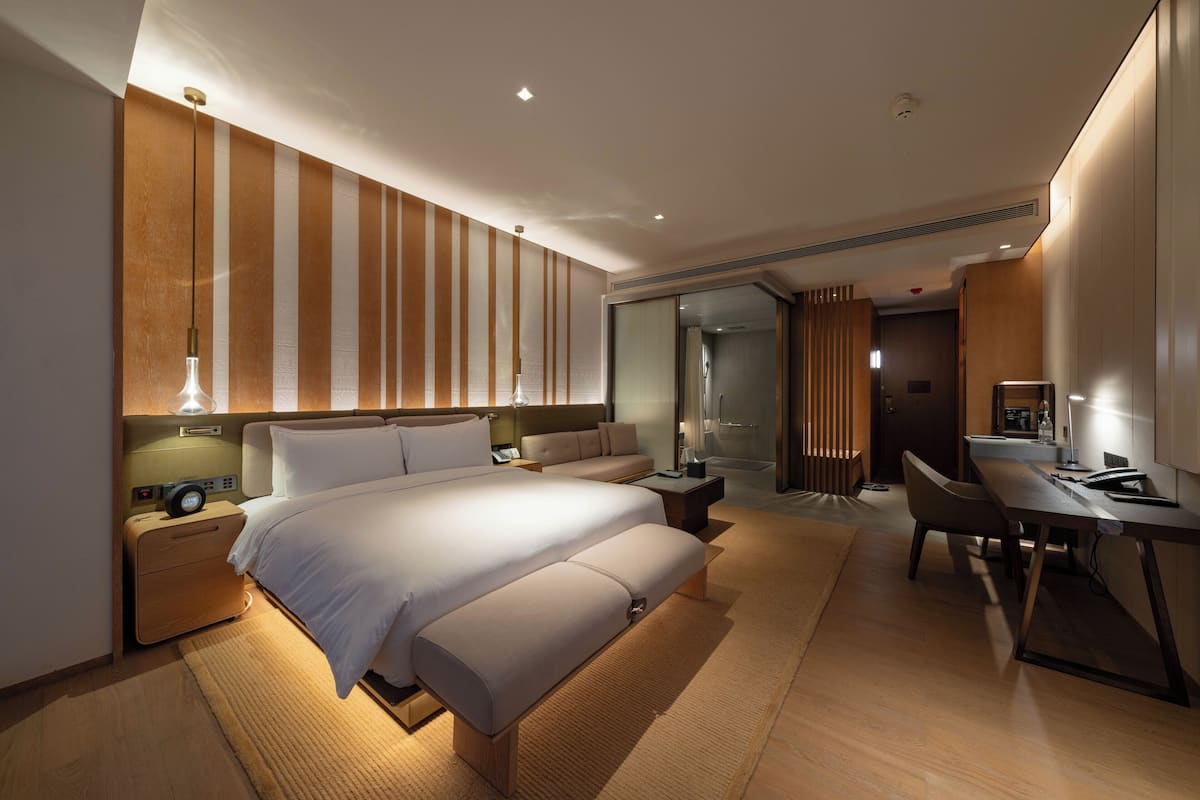Une chambre d’hôtel moderne avec un grand lit, un bureau, une chaise et une douche en verre.