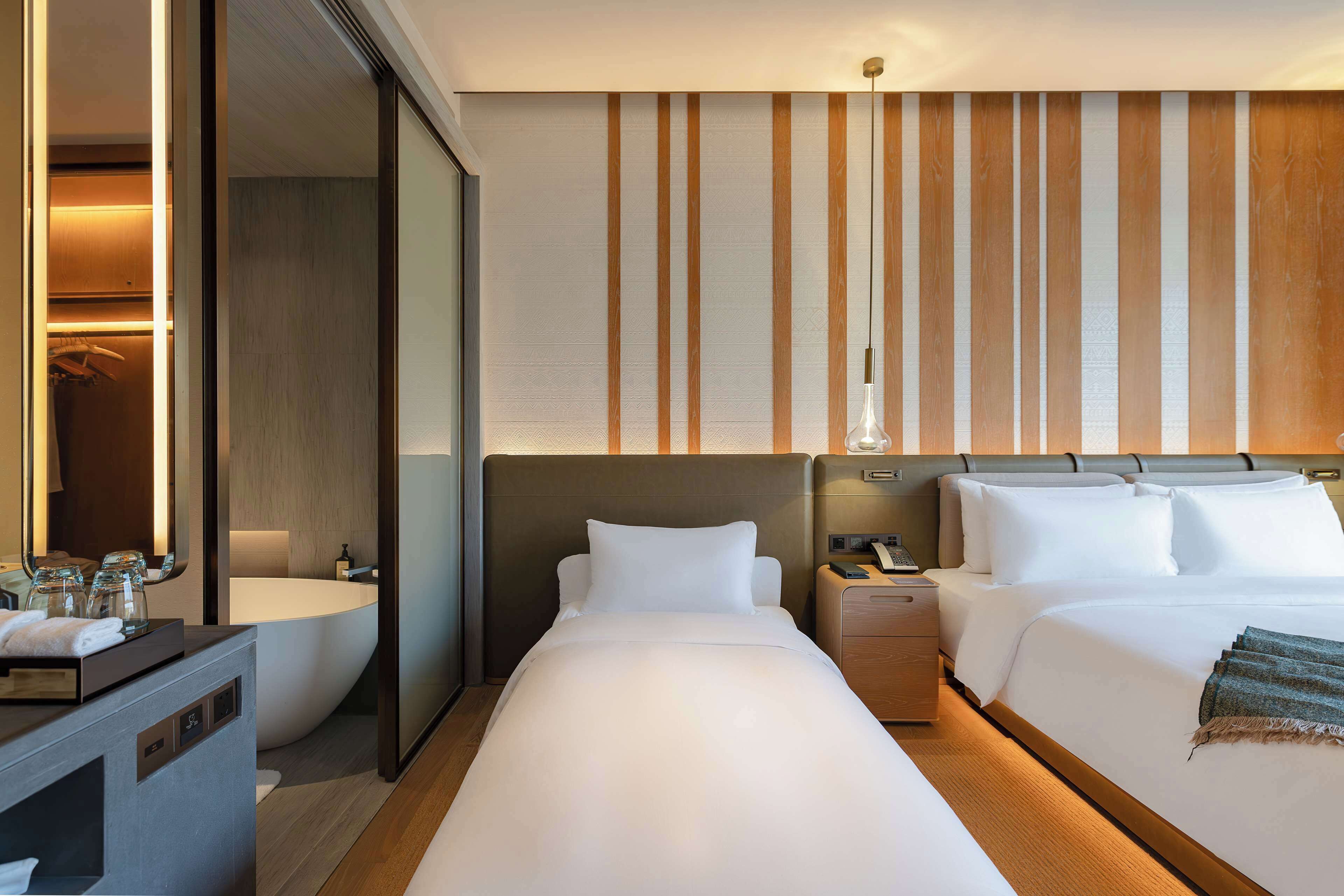 Quarto de hotel com uma cama grande, uma mesa de cabeceira, um banho com banheira e um espelho.