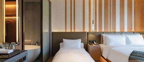 A hotel room with a large bed, a bedside table, a nightstand, a bathroom with a bathtub, and a mirror.