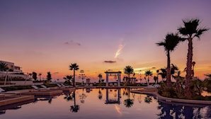 A resort pool with lounge chairs and palm trees at sunset.