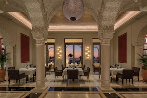A spacious dining area with high ceilings, large windows, and a view of the sunset. - Hilton Tangier Al Houara Resort & Spa (Hjar Ennhal)