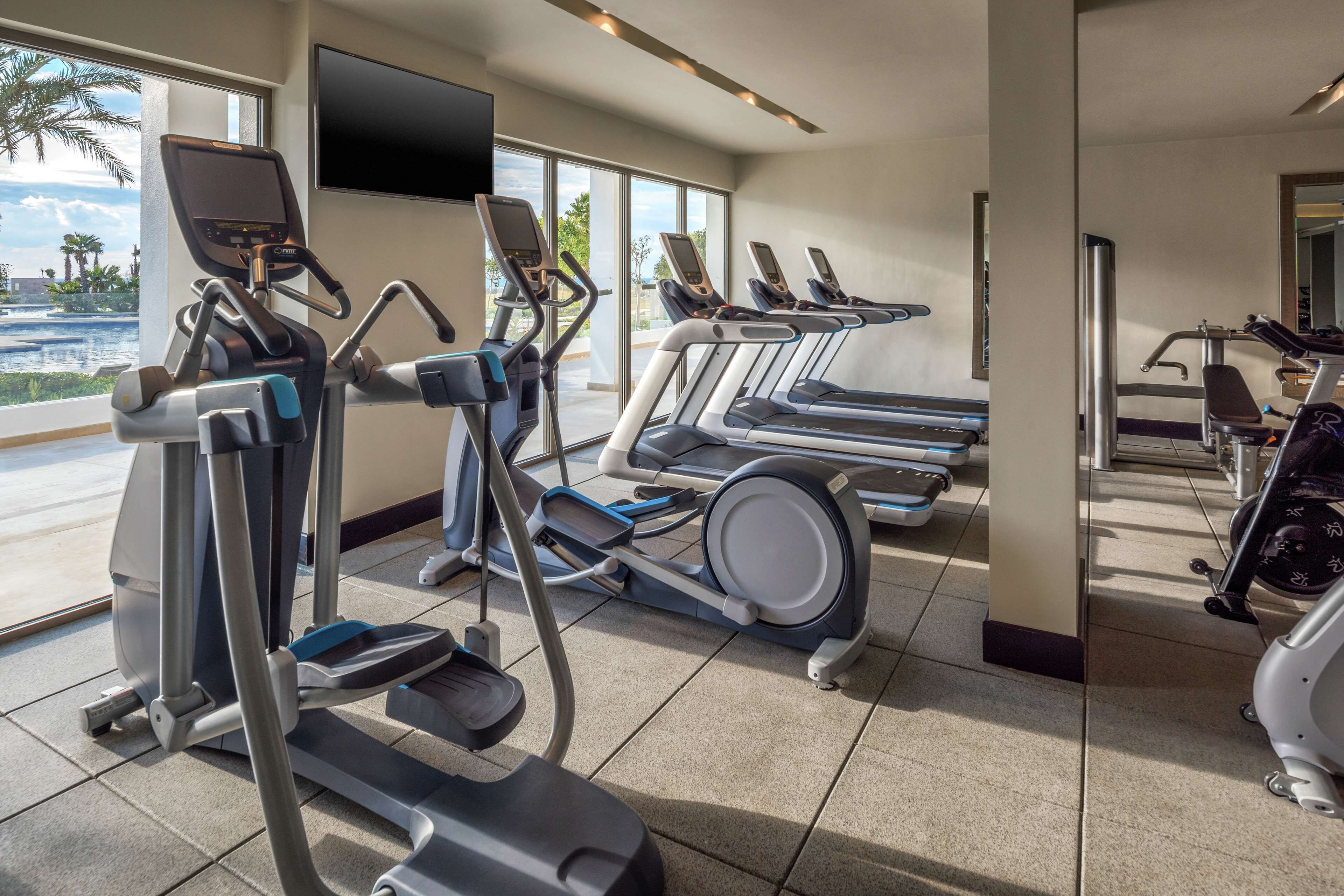 A gym with treadmills, elliptical machines, and a TV screen.