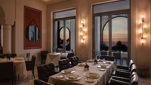 A dining area with tables set for a meal, large windows with decorative screens, and wall-mounted lighting.